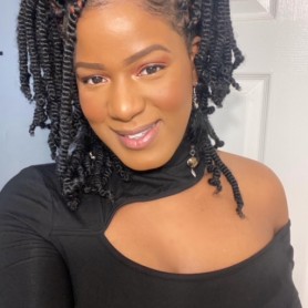 Photo of Antoinette Stewart shows her wearing an asymmetrical black top and long dangling earrings. Her short twisted hair is arranged in a half-up/half-down style.