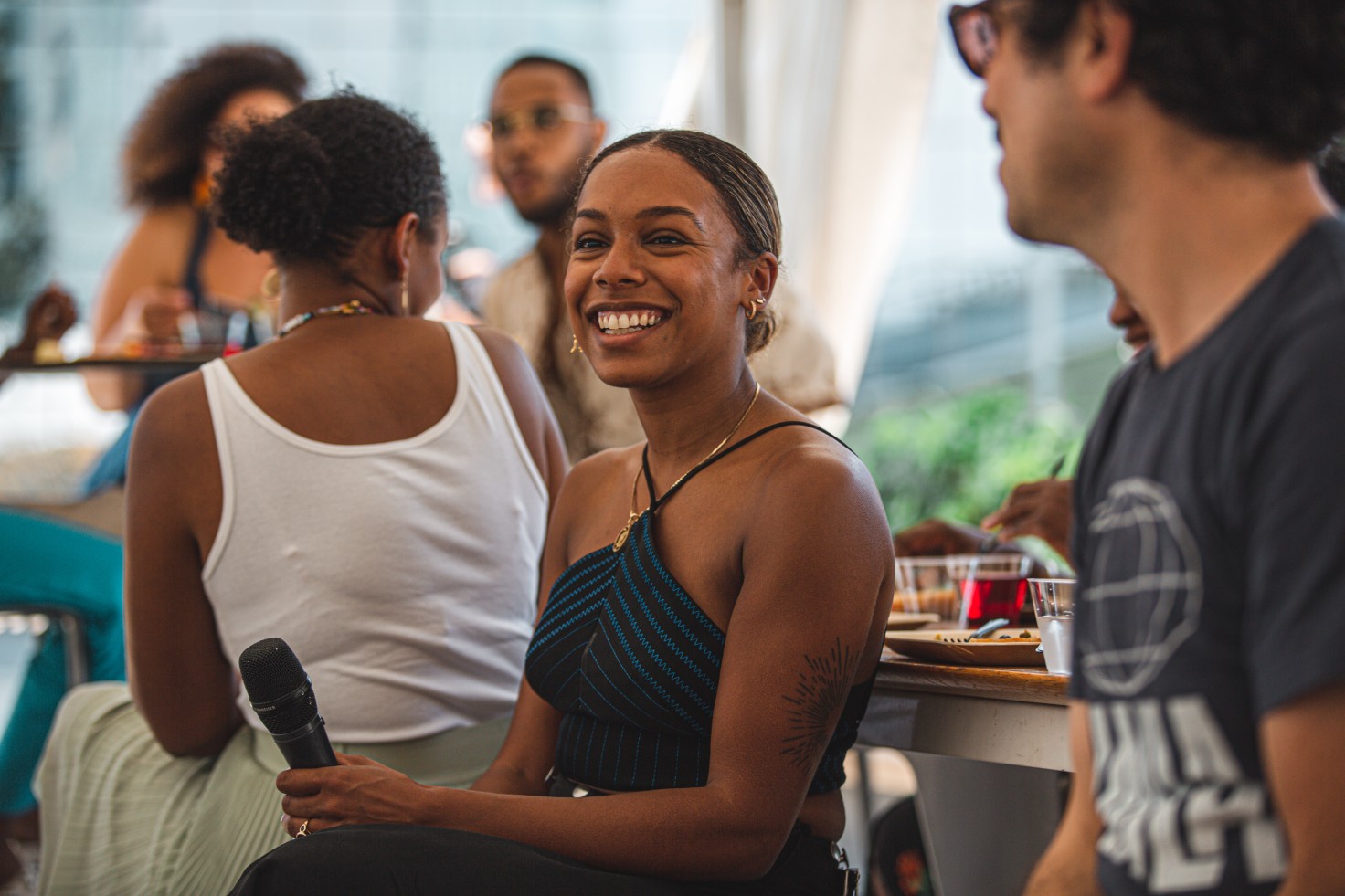 A photo of a person seated at the Directors' Brunch. They are holding a microphone and smiling.