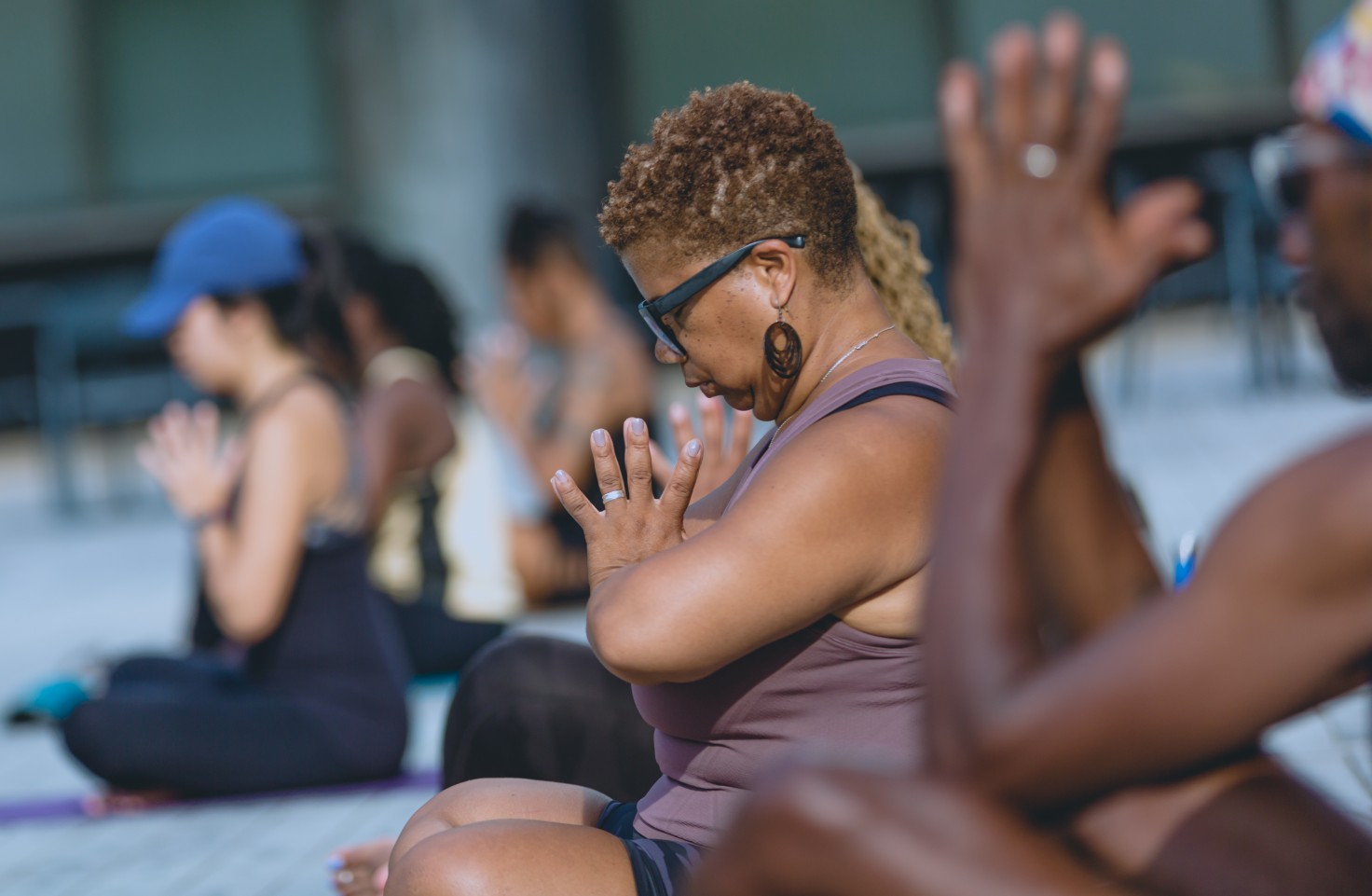 A photo of a yoga session. Three people are seated with the palms of their hands together, their heads are bowed.