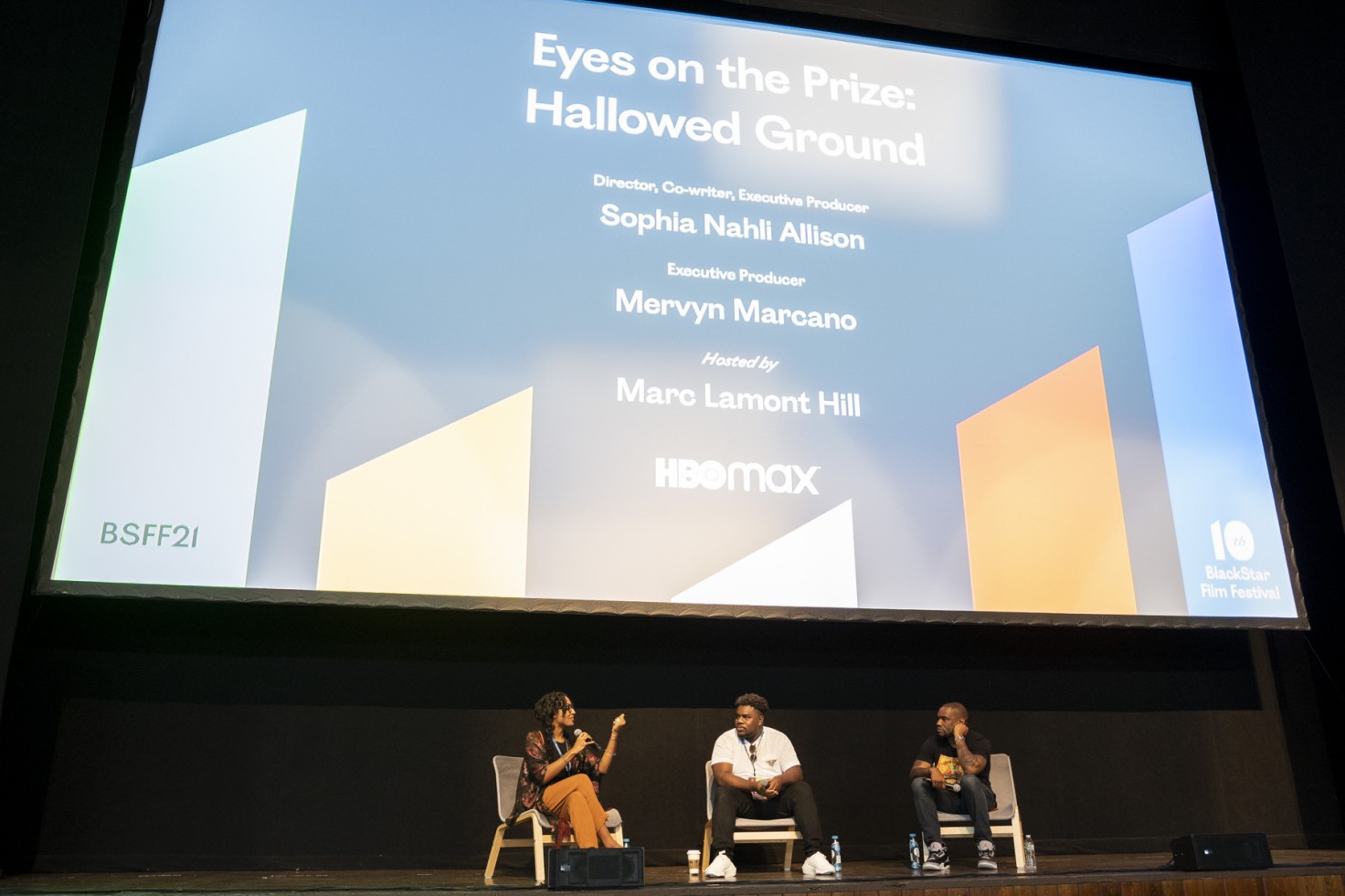 A photo of three people on stage in front of a large screen that says "Eyes on the Prize: Hallowed Ground."