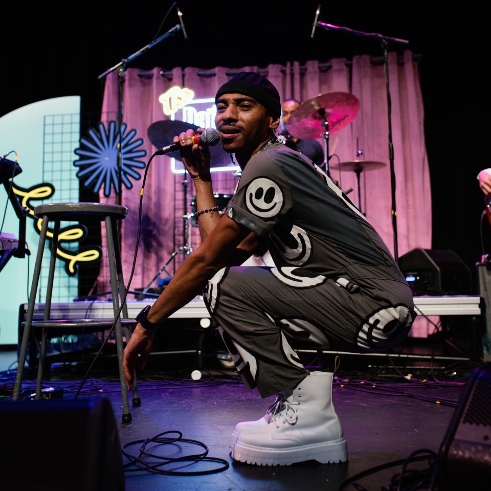 Singer Durand Bernarr is swatting on the set of the Daily Jawn, he is holding a microphone and singing.