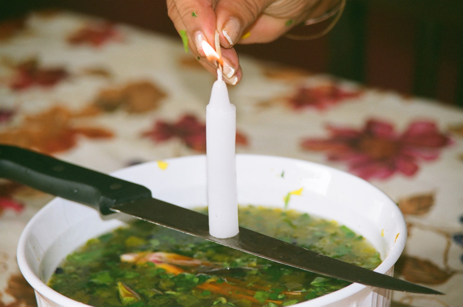 A photo of a bowl of soup, there is a steak knife laying across the bowl. Balanced on the knife is a candle. The candle is being lit.