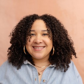 A headshot of Amber Hunnicutt, she is a Black woman. She has curly hair and is wearing gold hoops.