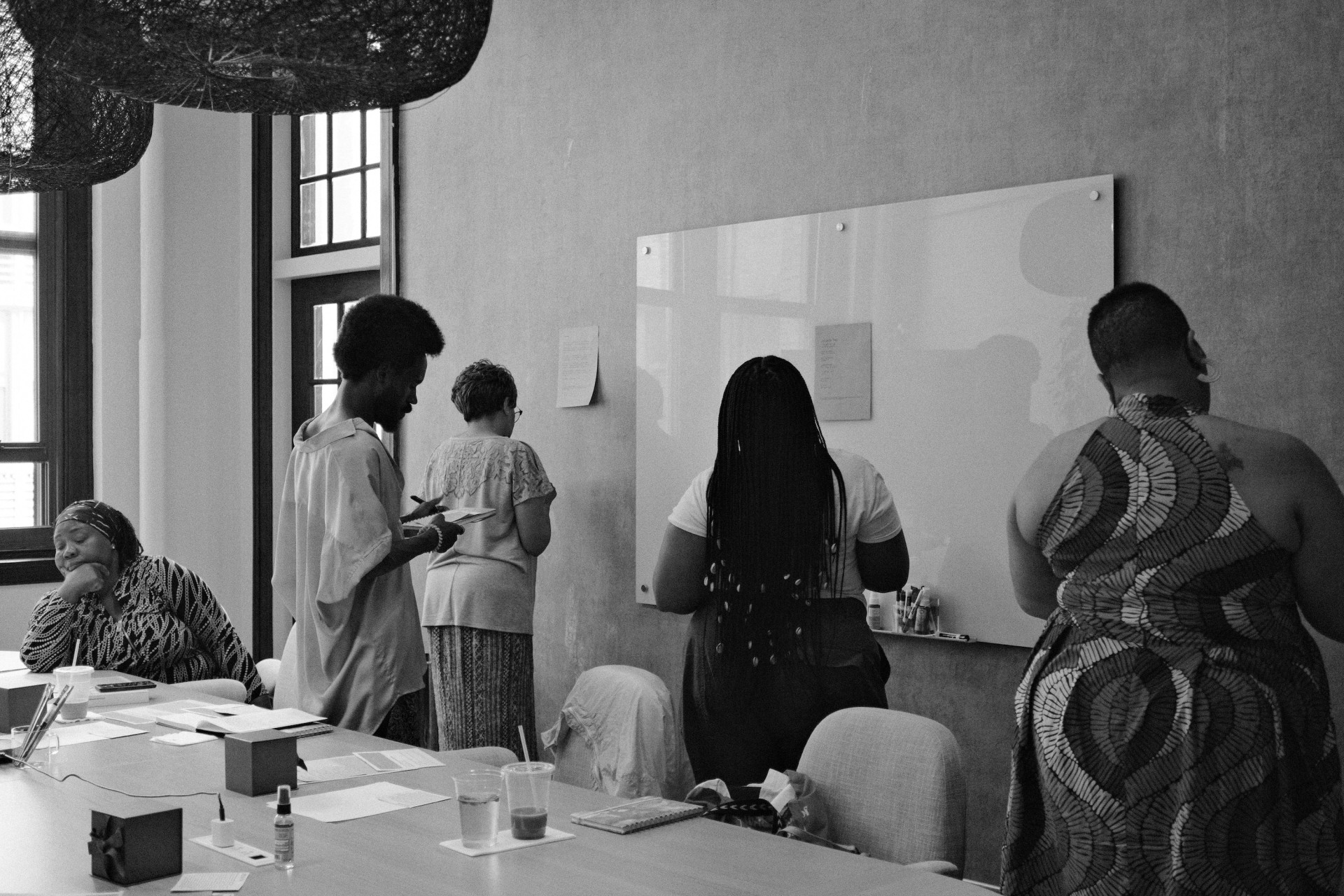 A black-and-white photo of a group of people in a meeting room, they are looking at a white board and appear focused.
