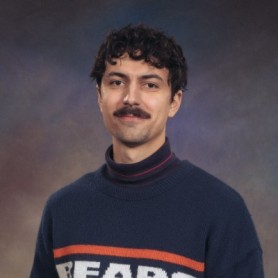 A picture of a man named Charles Frank. He has curly dark hair with a mustache and is centered against a backdrop of a smooth gradient transitioning from dark brown to purple hues. He has a calm and slightly smiling expression. He is wearing a dark blue sweater with the word "BEARS" in bold letters, highlighted by orange and white stripes. Underneath the sweater, he has a black and pink striped turtleneck.
