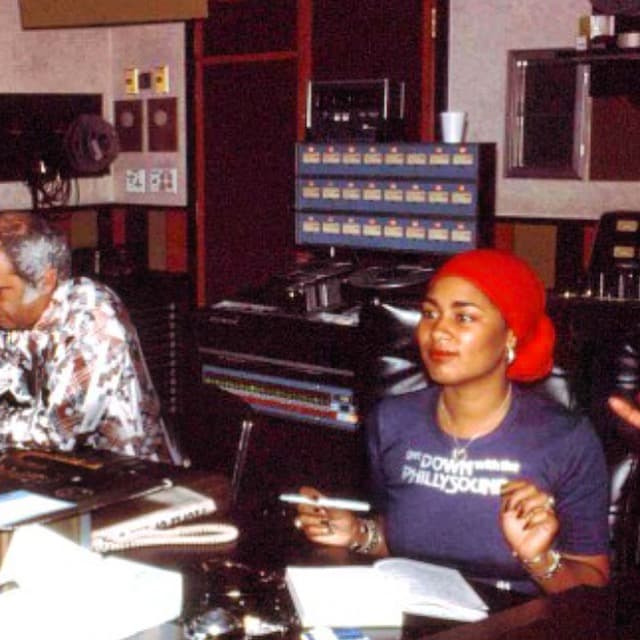 An old photo of two people seated in presumably a recording studio. One is a Black woman with a red headwrap.