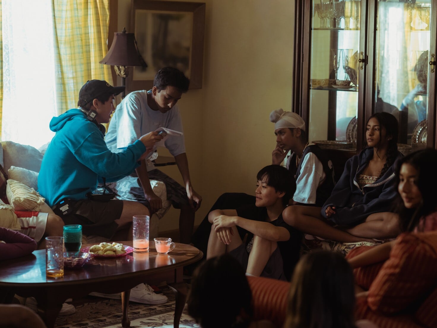 A behind the scenes shot of a group of child actors from “Didi” sitting in a living room, listening to director Sean Wang speak.