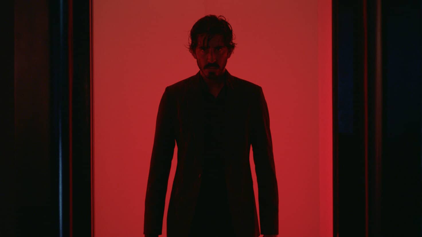 A still image from “Monkey Man” showing Kid (played by Dev Patel) backlit by red lights.