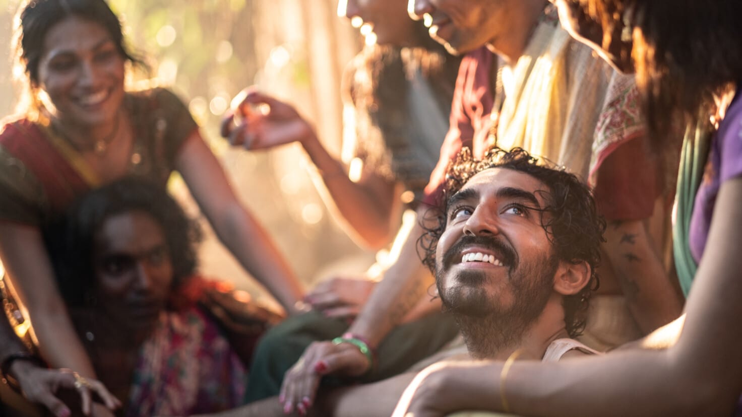 Kid looks up and smiles while surrounded by a group of hijra in “Monkey Man.”