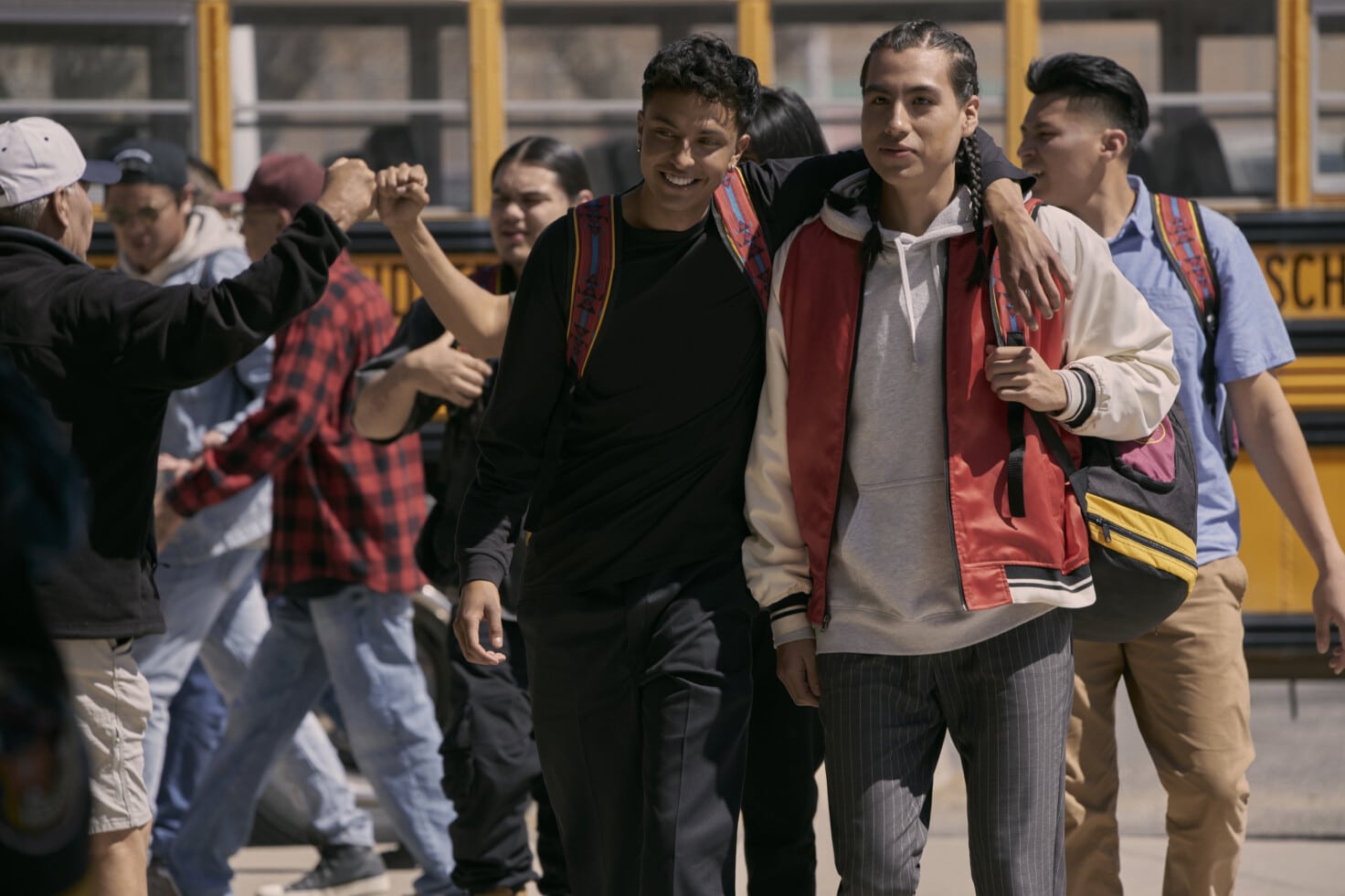 In the bottom half of the page, in a still from “Rez Ball,” Nataanii and Jimmy stand in front of a school bus with their teammates behind them.