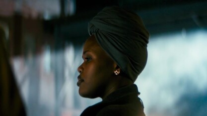 A poster from Adamstown shows three film stills stacked vertically. The top film still shows the side profile of a Black woman staring at something off screen. She is wearing a green scarf tied in a knot on her head and gold earrings against a blurred out background. The middle film still shows a figure dressed in all black running through a dimly lit room. On both sides of the figure are metal gates lining the wall. The bottom film still shows the silhouette of a person walking from the darkness into a window-lit room. To the right of the silhouette is a door with closed shades on the glass.