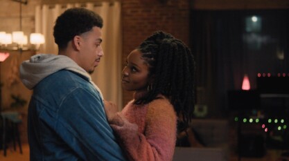 A film still from Food for the Souls shows a young Black woman and man in an embrace sharing a gaze.