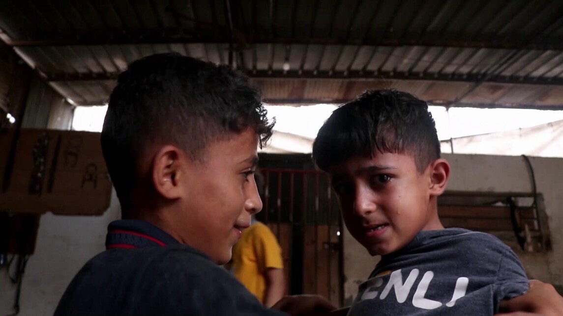 A film still from Gazan Tales shows two young boys. The boy on the left looks toward the boy on the right, who gazes into the camera with teary eyes and a single tear trailing down his cheek.