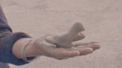 A film still from Images de Tunisie shows the palm of a hand covered in clay that holds a clay figure.