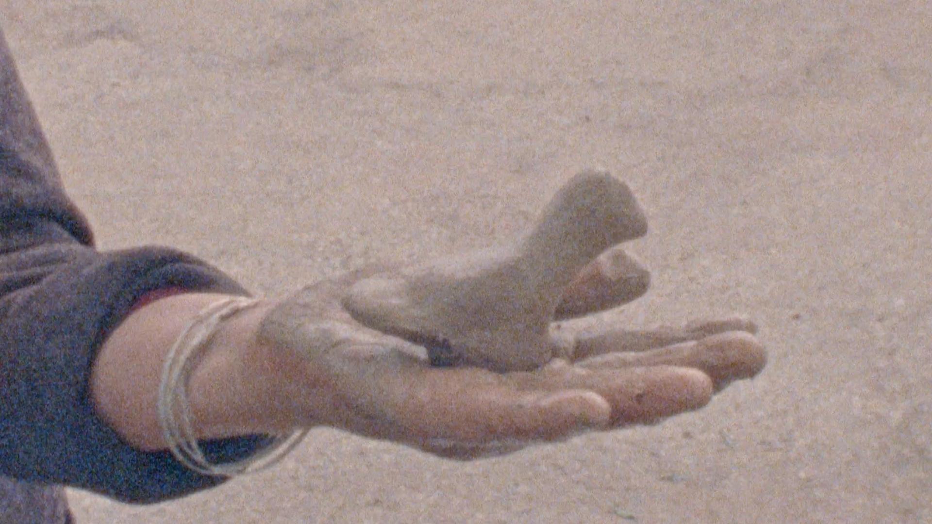 A film still from Images de Tunisie shows the palm of a hand covered in clay that holds a clay figure.