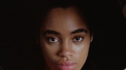 A film still from Seek No Favor shows the face of a Black woman who looks directly into the camera with a straight face.