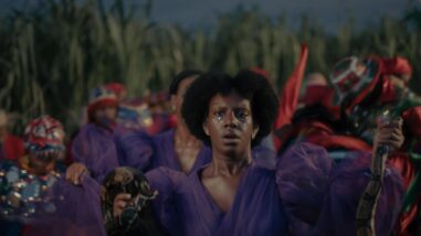 Makenya is wearing a purple dress holding a staff on one hand and a brown snake in the other