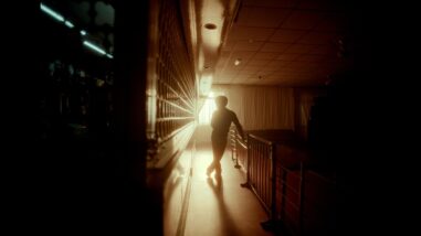 A film still from The Great North shows a silhouette standing in the center of a dark room, illuminated solely by a window whose curtain is pulled open. The silhouette is positioned between a railing and a wall that extends to the camera. The other side of the wall reveals a dimly lit room with indiscernible items.