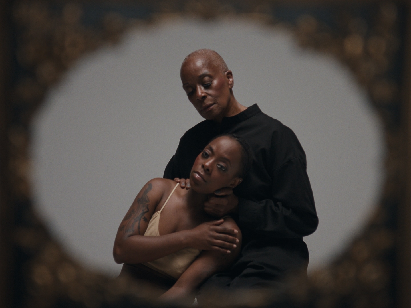 An image of two older Black people holding one another. Around the edges of the image is an oval frame.