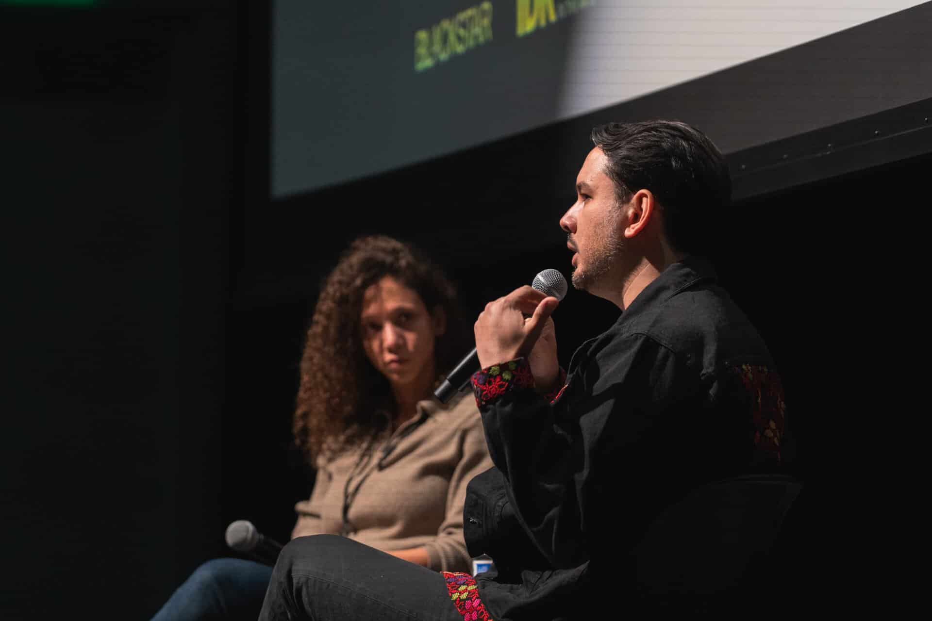 A photo of Suneil Sanzgiri in conversation with someone. They are on stage, both people are holding microphones.