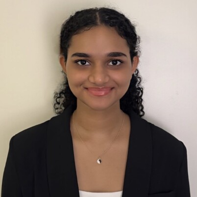 A headshot of a young woman. She is wearing a black blazer, a white top, and is smiling at the camera.