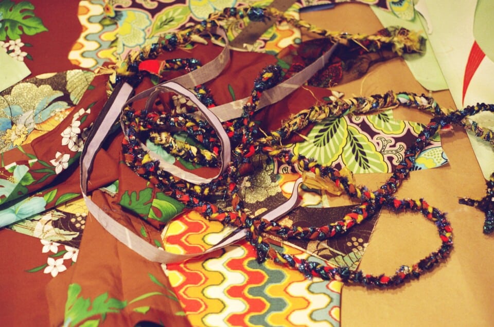 Colorful pieces of yarn and string that braided artistically lay on top of assorted patterned fabrics.