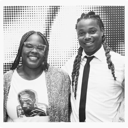 A black-and-white photo of Beandrea July and Kendale Winbush standing arm-in-arm. Beandrea is wearing a t-shirt with an image of James Baldwin.