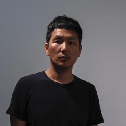 A headshot of Tenzin Phuntsog. He is an Asian man, is a wearing a black shirt and is looking directly at the camera.