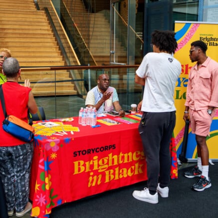 A photo from a past BlackStar Film Festival of Storycorp tabling. There are people gathered around smiling.