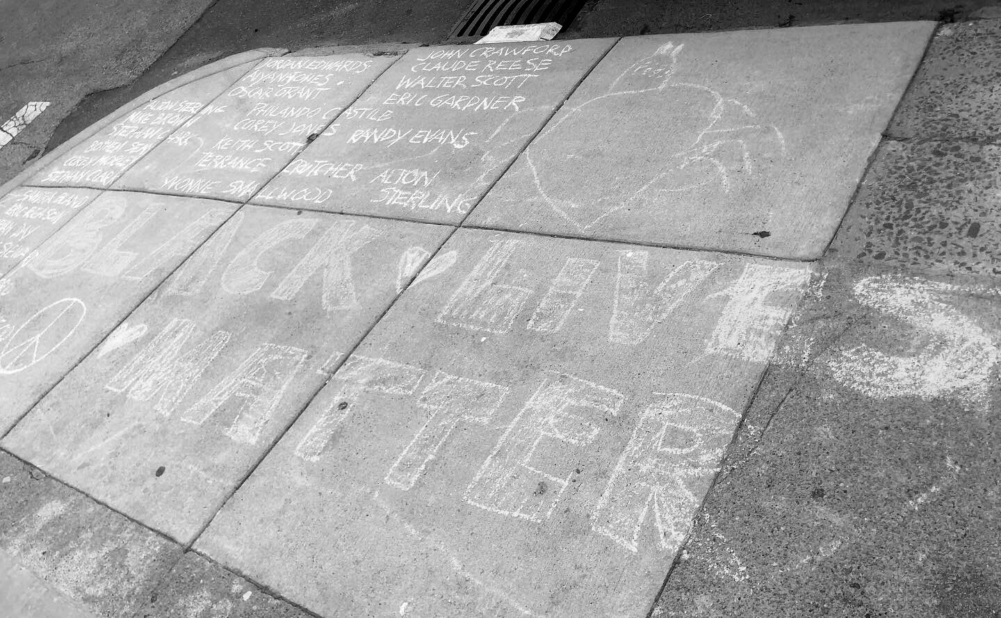 "Black Lives Matter" written out in chalk on a sidewalk in Philadelphia, above the phrase are the names of Black individuals who have been killed by the police.