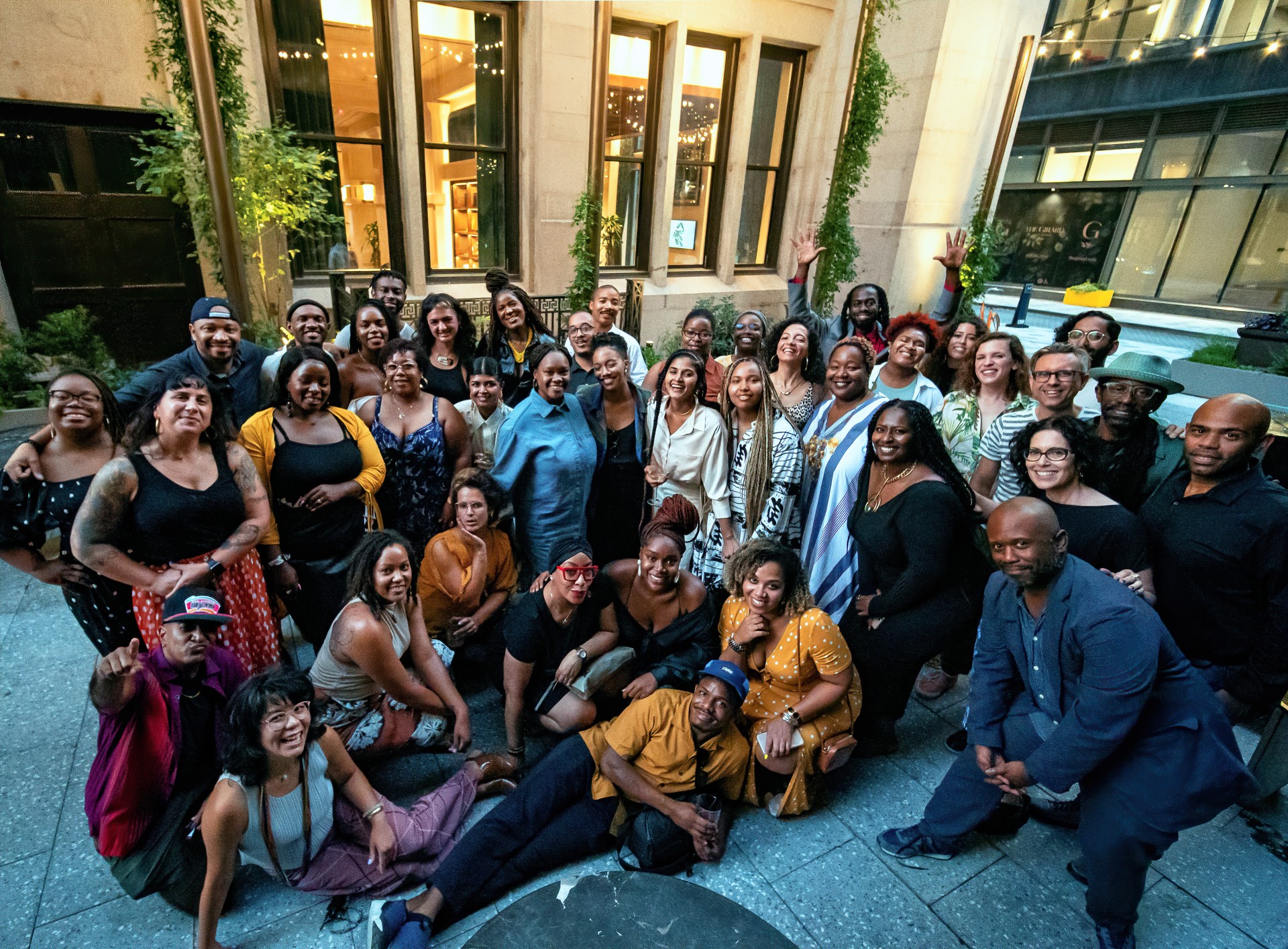 A group photo of festival staff, year-round staff, and board taken at the conclusion of the 2021 BlackStar Film Festival. It shows the group huddle together and posing for the camera, which is slightly above the crowd. Most people are smiling widely and there are a number of bright colors worn. It is taken outside in the early evening.