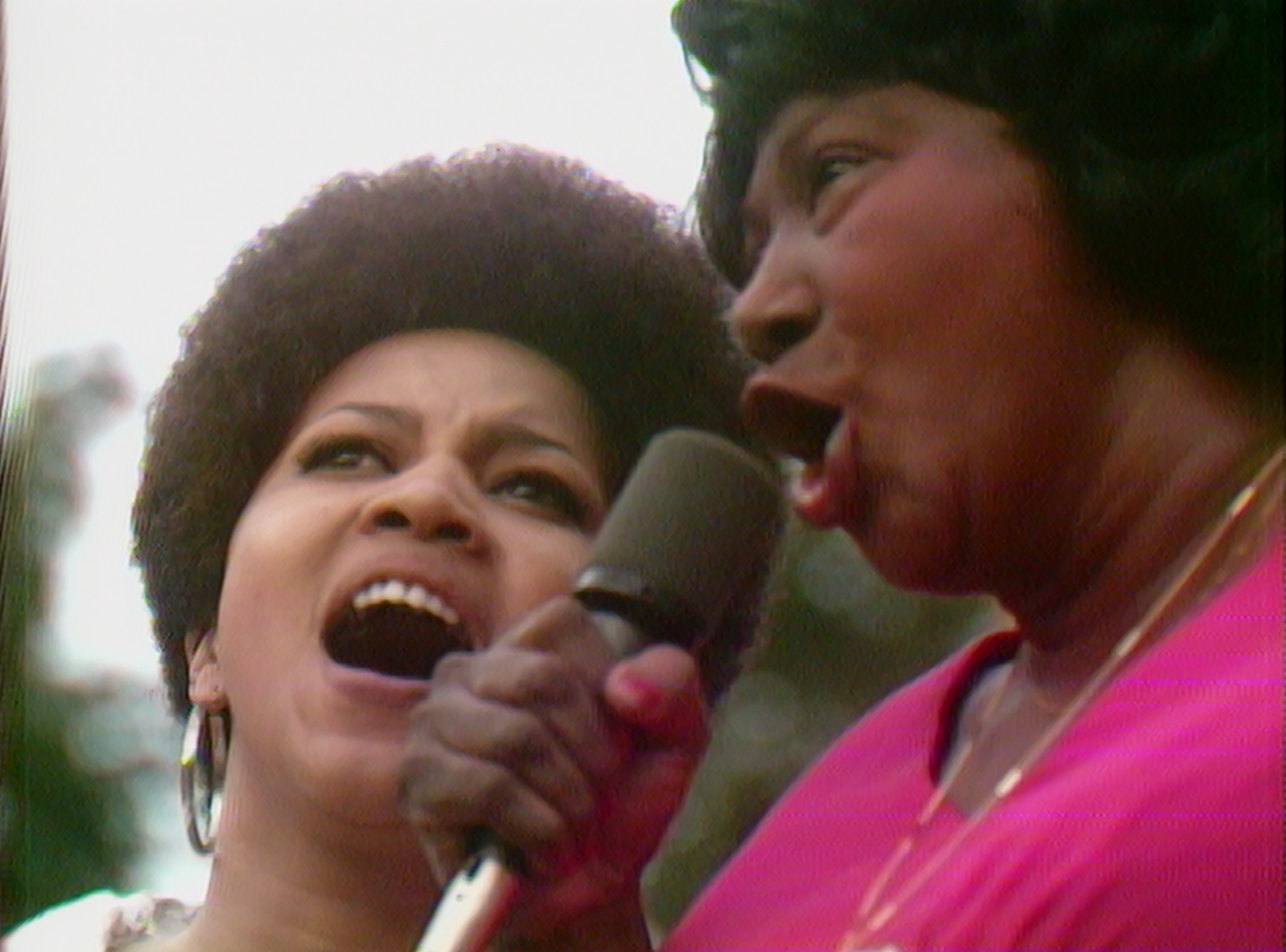 Still from the film "Summer of Soul" is a close-up image of two Black women singing into a microphone.