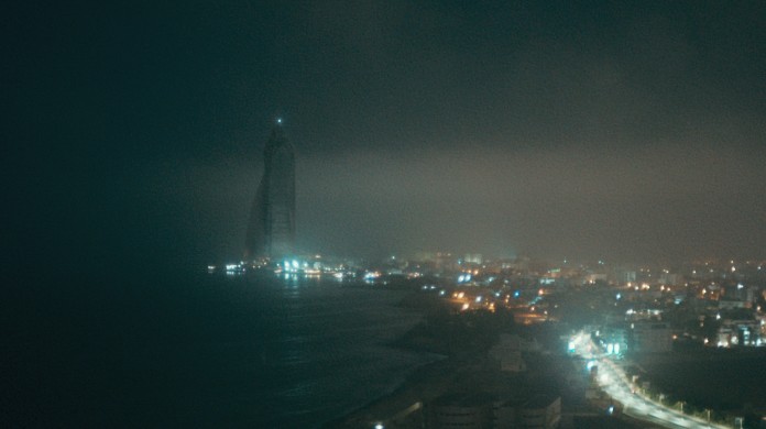 Still from the Film Atlantics shows a dark coastline illuminated by bright city lights.