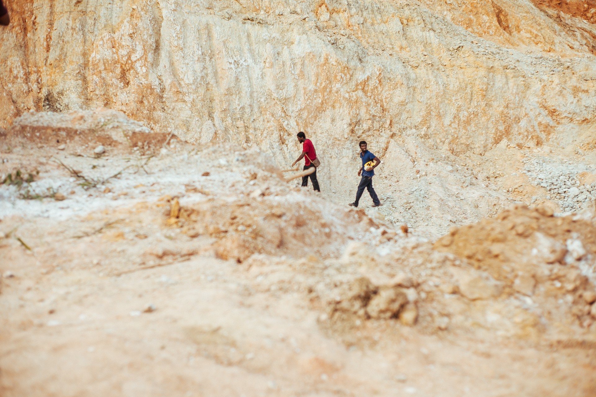 Still from the film "The Burial of Kojo" shows two figures walking in a rocky canyon area. With the tan canyon walls and floor, their clothes and skin seem to stand out brightly.
