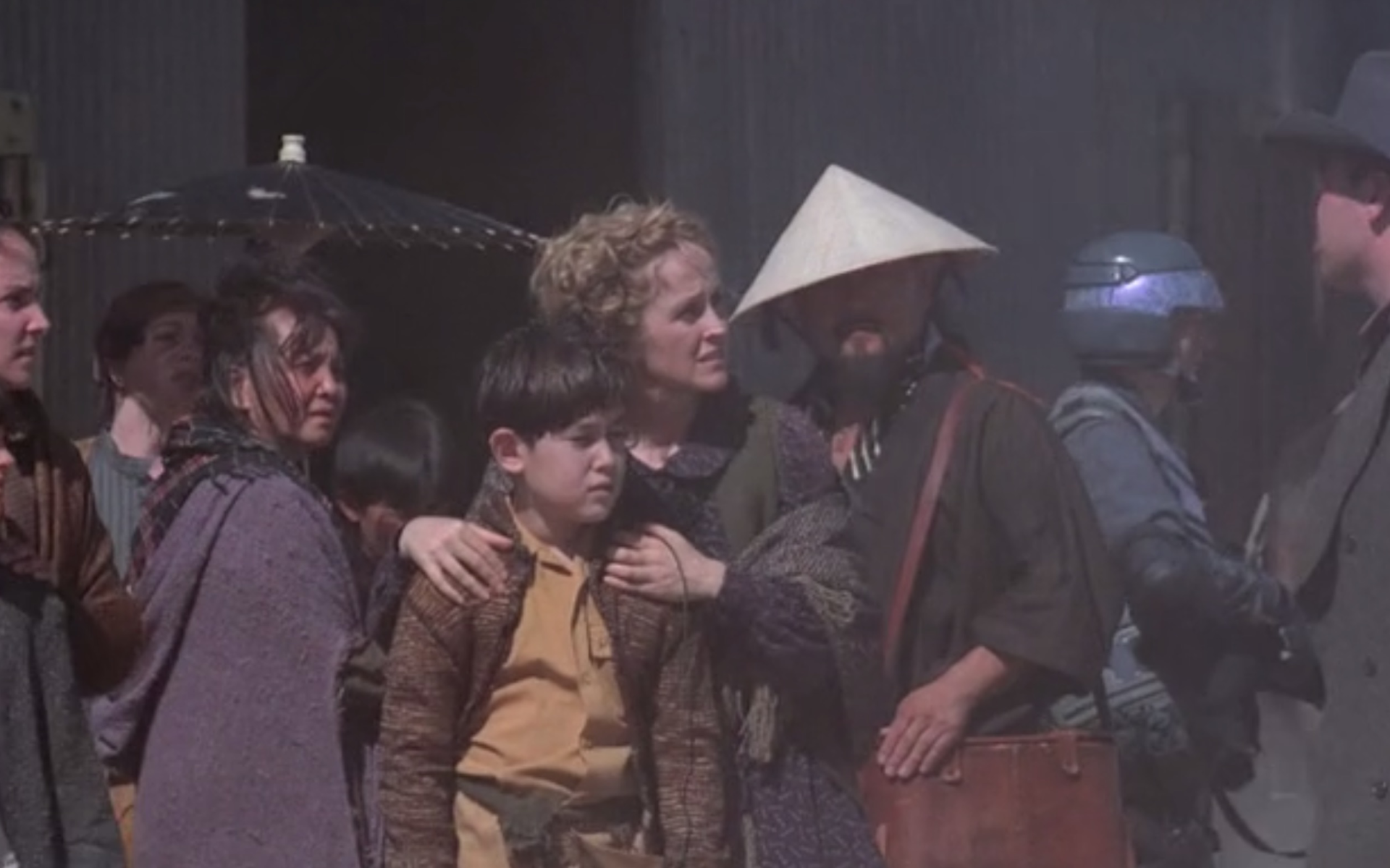 Still from the series "Firefly" shows a group of people standing and looking around. They wear mostly earth-toned clothes. One person wears a conical hat.