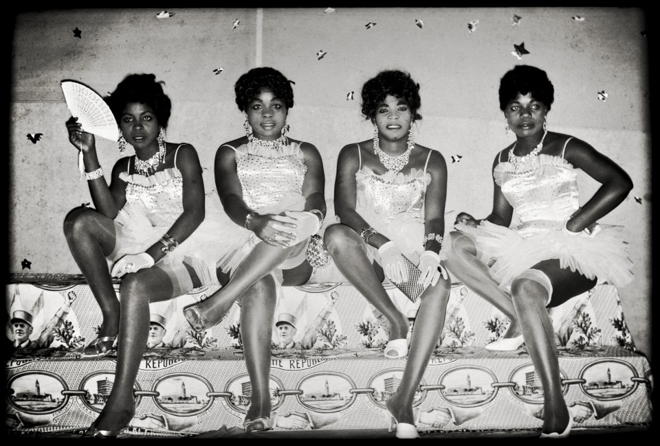 Four dancers sitting on a platform, Kinshasa, ca. 1955-1965. All are Black and wear dresses.