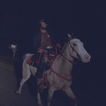 A still from When I Get Home. A Black man is riding a white horse down a road at night.