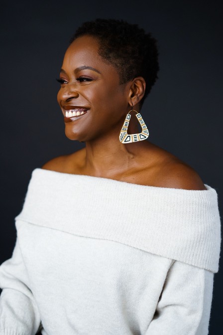 A headshot of Yaba Blay smiling. Yaba is wearing a white off-the-shoulder top and chunky earrings.