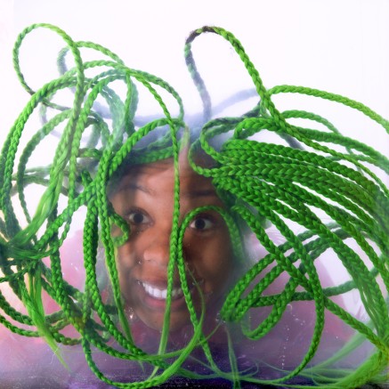 A photo of Martine Syms. Her green braids are falling in front of her face.