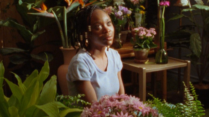 A still from CETTE MAISON, featuring a Black person sitting amongst flowers and greenery, inside.