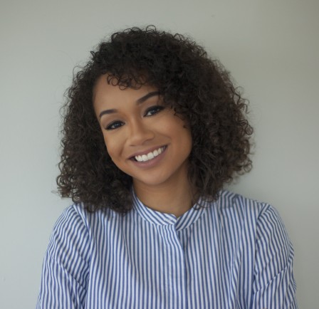 A headshot of Deniese Davis. Her curly hair is framing her face, she is smiling, and her head is tilted slightly to the left. She is wearing a pins-striped blouse.