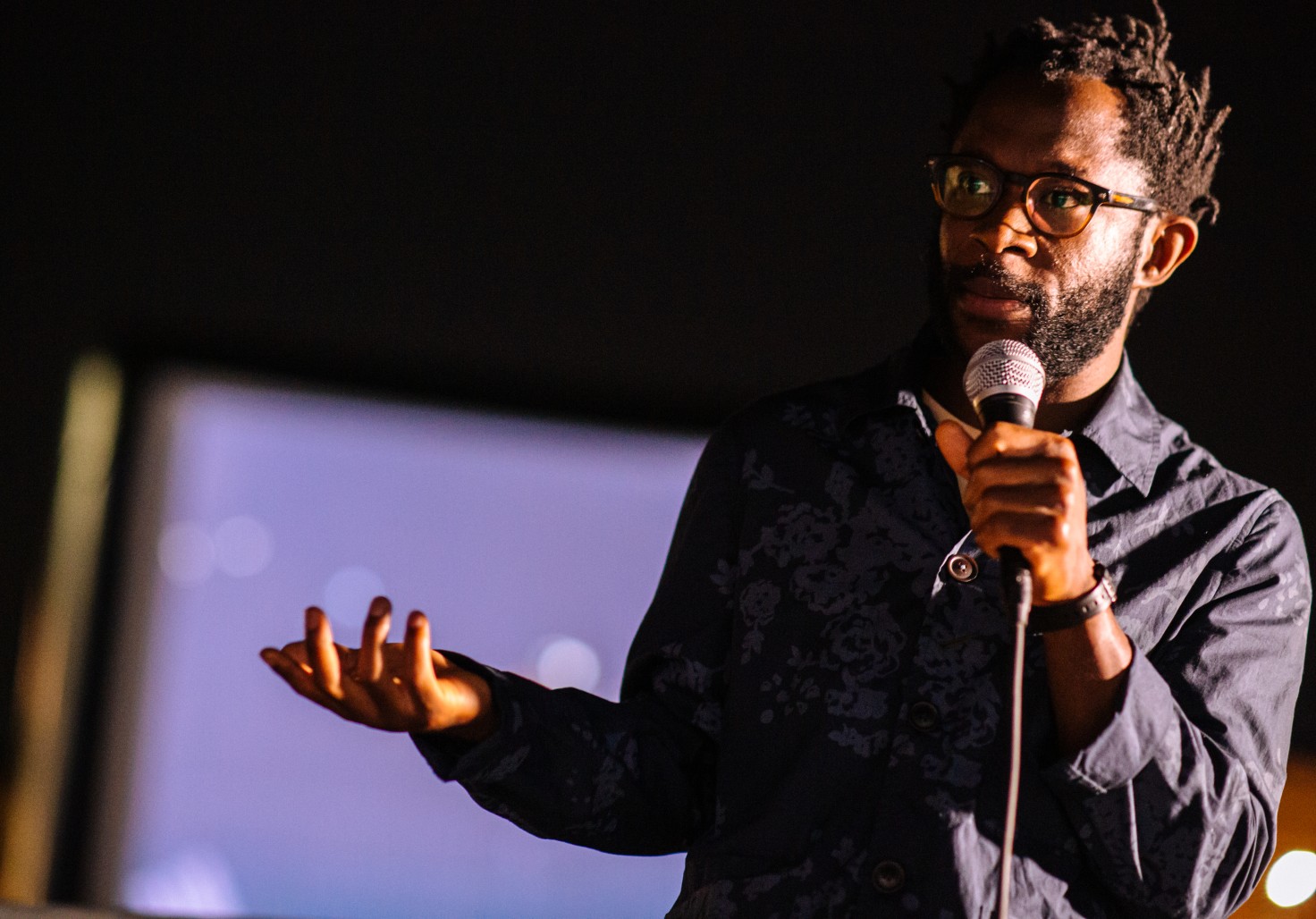 A photo of a Black man speaking into a microphone.