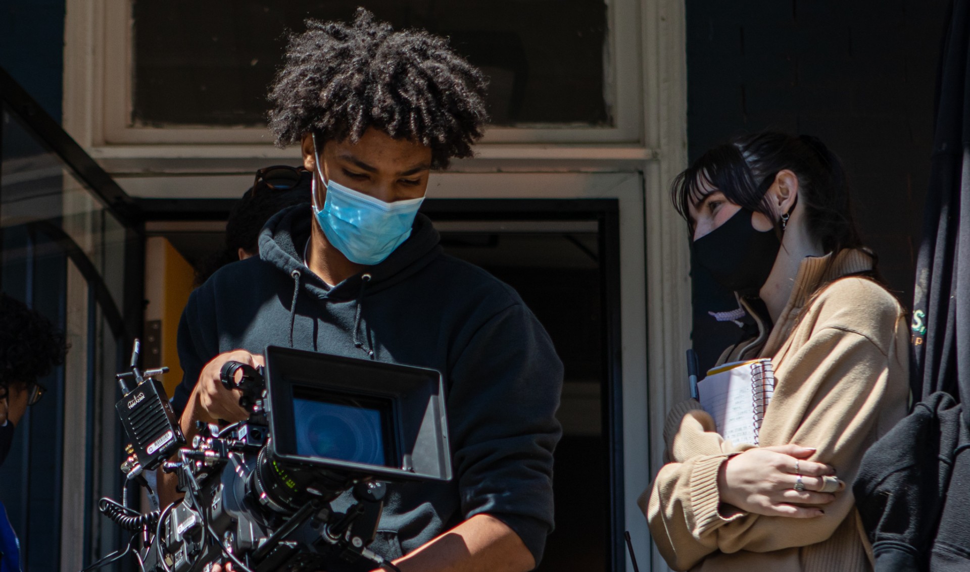 A Black person is on a film set holding a camera.
