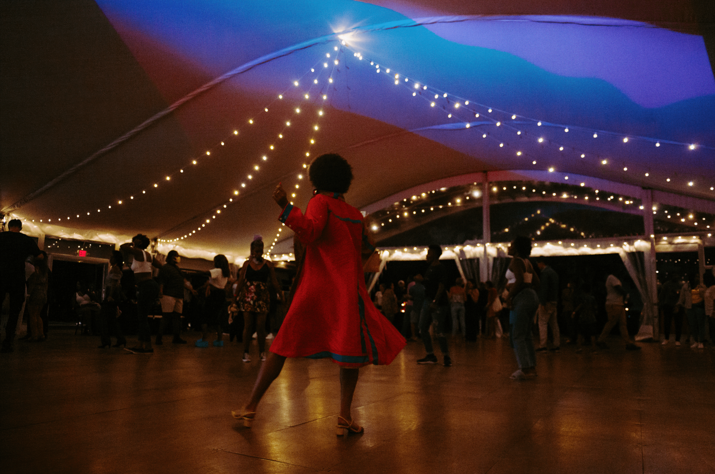 A photo of a person in a red dress with green strips in the middle of a dance floor. There are other people around them. Everyone is dancing.