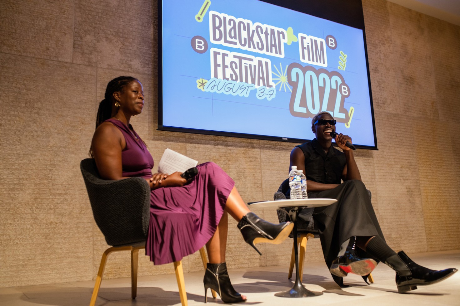 Moses Sumney and Iyabo Kwayana sit on stage in front of a screen with the BlackStar Film Festival flier.