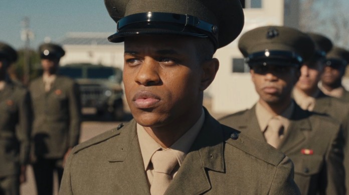 A still from The Inspection shows a Black man looking concerned, pensively at something off screen while standing in uniform in line with other military members.