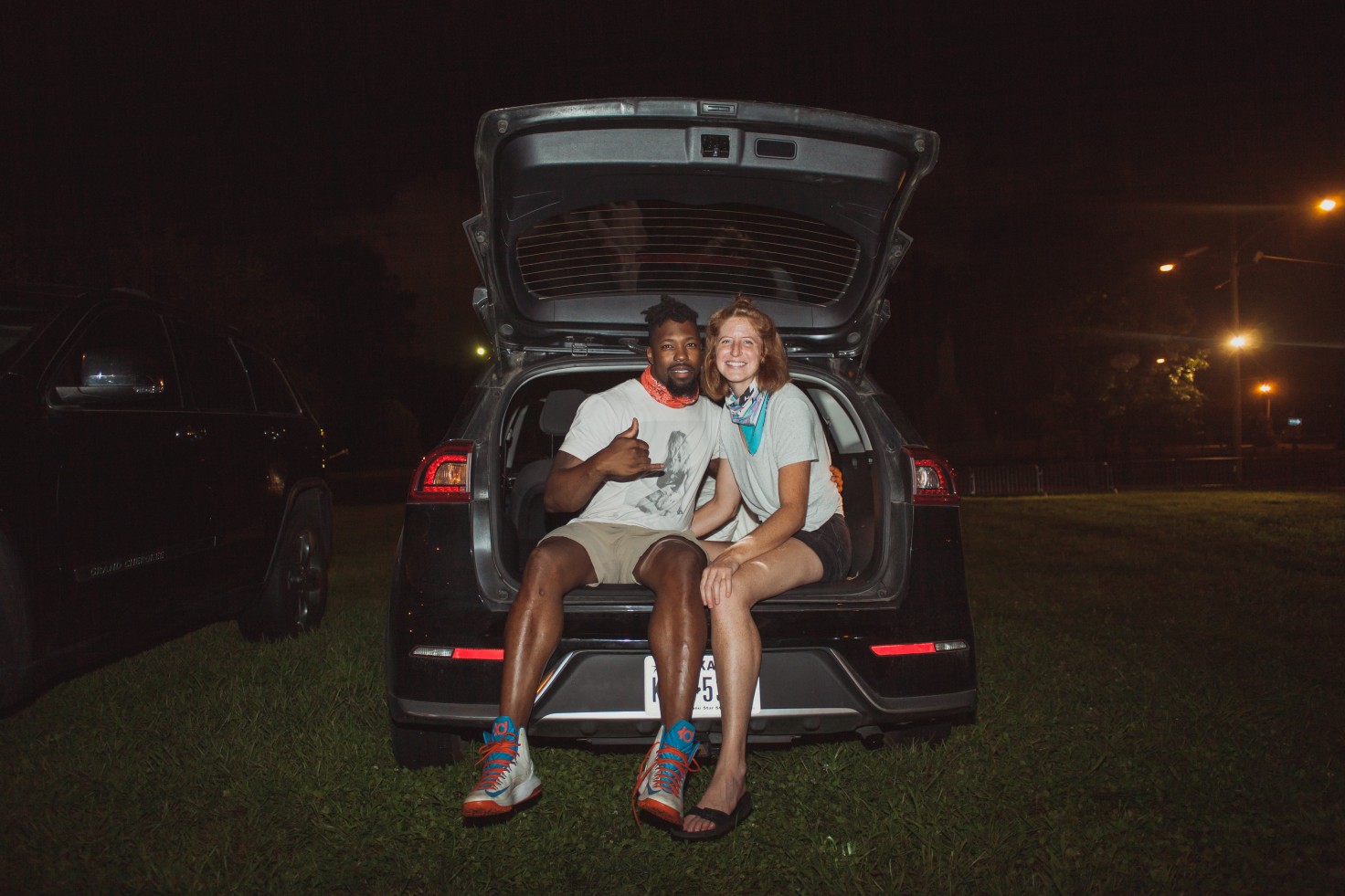 A photo of two people sitting in the truck of their car. They are smiling for the photo.