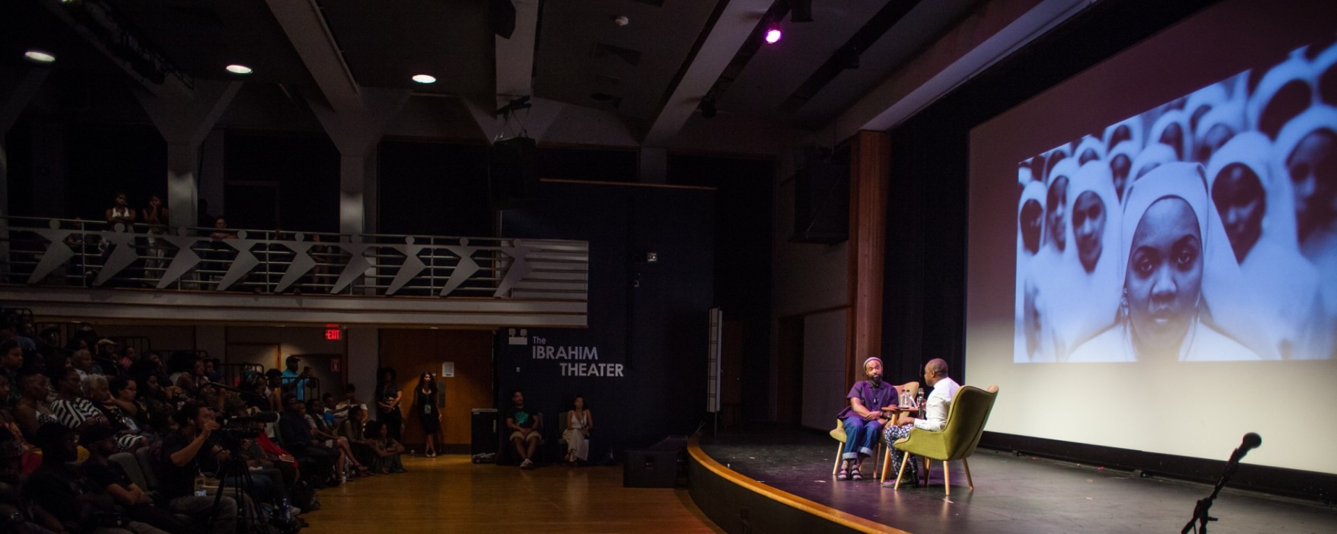 A photo of two people on stage in conversation. There is a packed audience listening in.