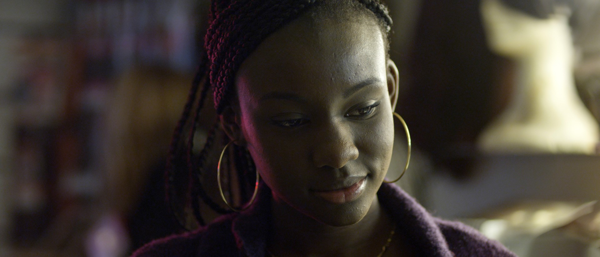 A still from the film UNIVITELLIN by Terence Nance shows a Black person's face in close-up, they are almost smiling and wearing large gold hoop earrings - looking down.
