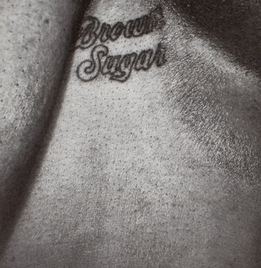 A close-up photo of a person's chest. Between their breasts is a tattoo that says "brown sugar."